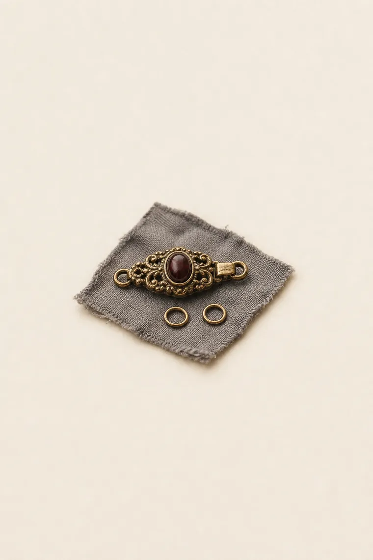 Cierre decorativo de collar de oro viejo y dos anillas apoyados sobre un cuadrado de paño gris.