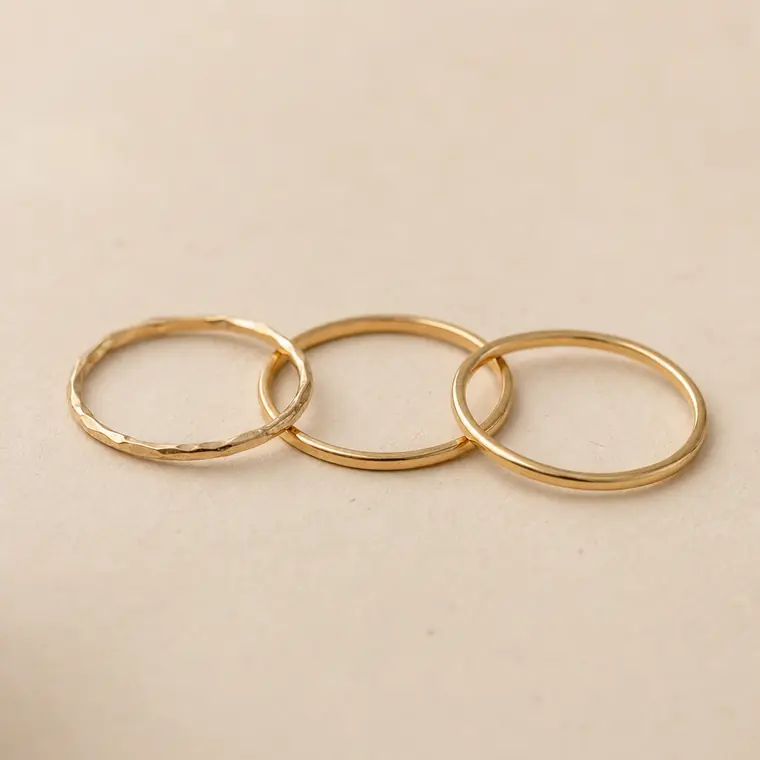 Tres anillos finos en metal dorado claro apoyados uno junto a otro sobre papel marfil.
